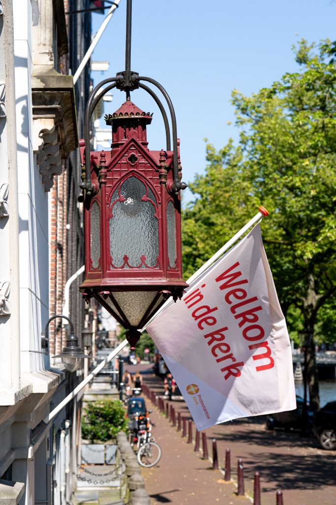 Vlag aan de gevel van de kerk met de tekst: Welkom in de kerk